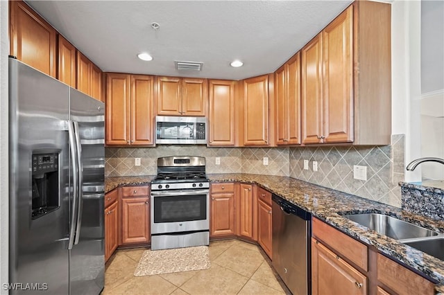 kitchen with light tile patterned floors, stainless steel appliances, visible vents, a sink, and dark stone counters