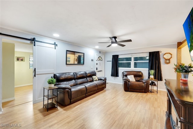 living room with a barn door, ceiling fan, ornamental molding, and light wood-type flooring