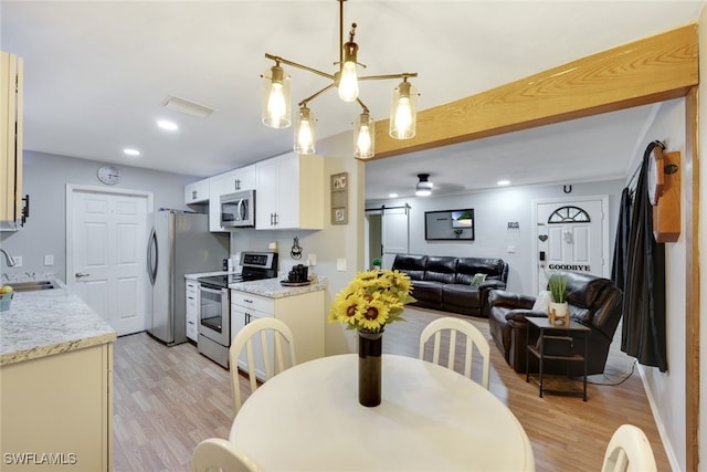 dining room with a barn door, ceiling fan, sink, and light hardwood / wood-style floors