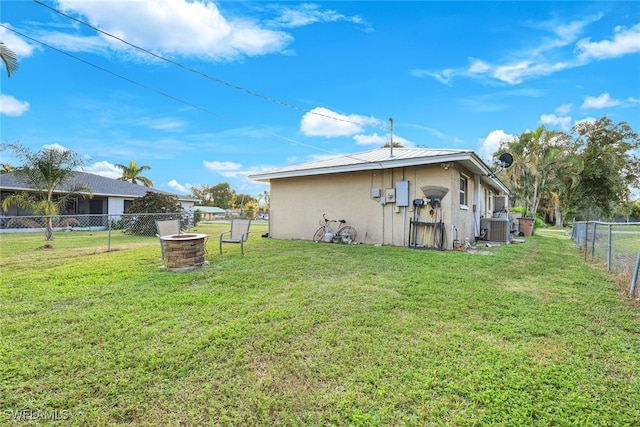 back of house featuring central AC unit, an outdoor fire pit, and a lawn