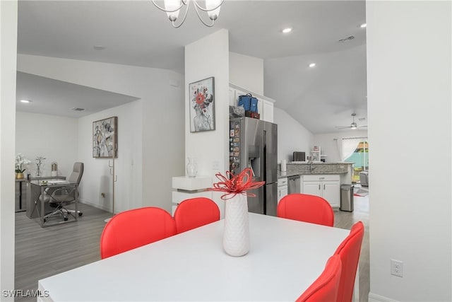 dining room with ceiling fan with notable chandelier, wood-type flooring, and vaulted ceiling