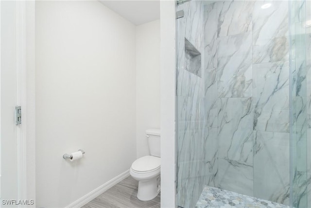 bathroom with hardwood / wood-style flooring, toilet, and a tile shower