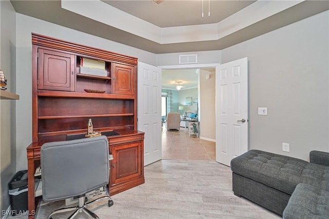 home office with a tray ceiling and light wood-type flooring