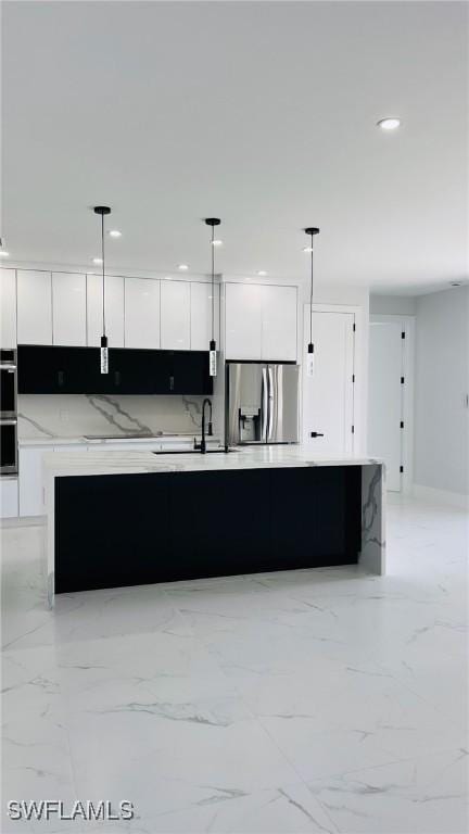 kitchen with pendant lighting, white cabinets, stainless steel appliances, and a center island with sink