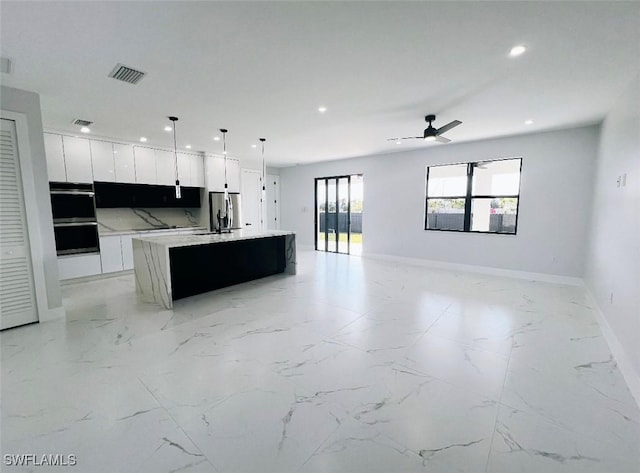 kitchen with white cabinetry, ceiling fan, hanging light fixtures, tasteful backsplash, and a center island with sink