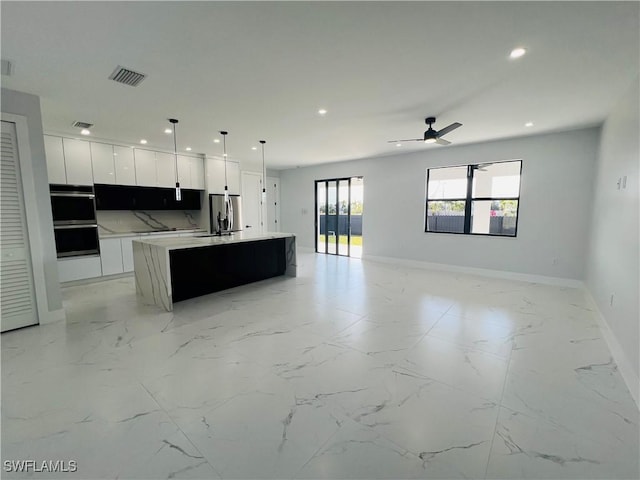 kitchen with decorative backsplash, ceiling fan, a center island with sink, white cabinets, and hanging light fixtures