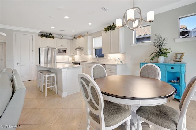 dining space with sink, an inviting chandelier, crown molding, and light tile patterned flooring