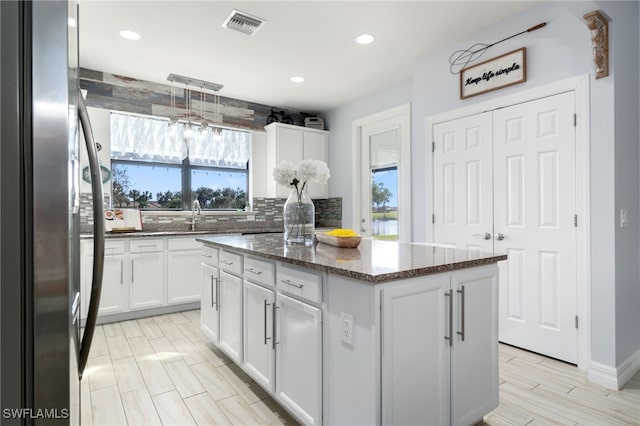 kitchen featuring white cabinets, plenty of natural light, a kitchen island, and stainless steel refrigerator