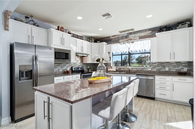 kitchen with white cabinets, appliances with stainless steel finishes, a center island, and dark stone counters