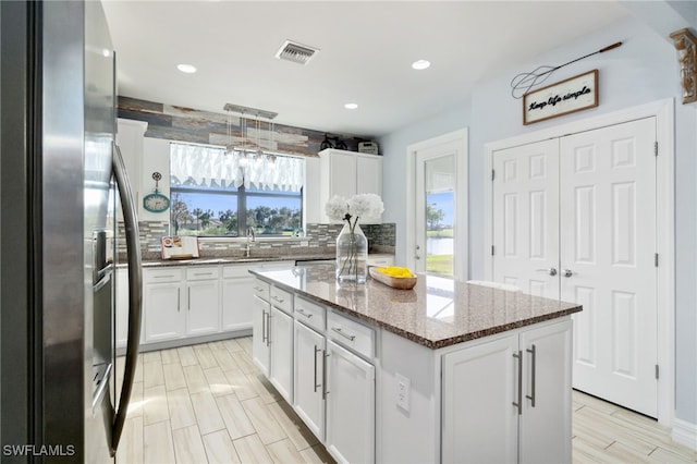 kitchen featuring white cabinets, decorative backsplash, decorative light fixtures, a kitchen island, and stainless steel fridge with ice dispenser