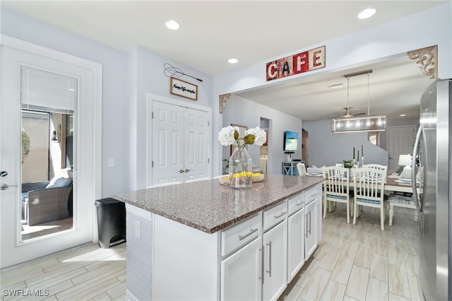 kitchen with stainless steel refrigerator, white cabinetry, a center island, dark stone counters, and decorative light fixtures