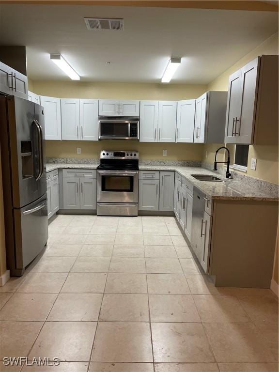 kitchen featuring light stone countertops, stainless steel appliances, sink, light tile patterned floors, and gray cabinets