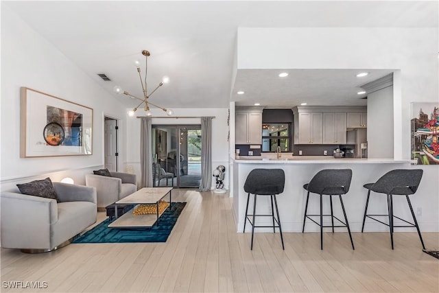 kitchen featuring kitchen peninsula, light wood-type flooring, gray cabinetry, a chandelier, and hanging light fixtures