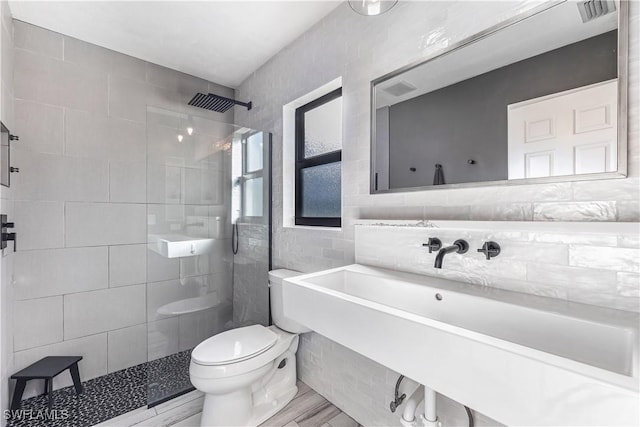 bathroom featuring hardwood / wood-style floors, toilet, a tile shower, and tile walls