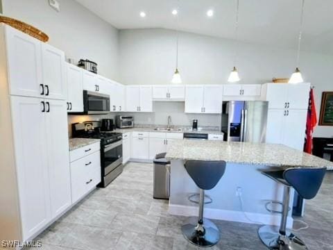 kitchen with white cabinets, decorative light fixtures, stainless steel appliances, and a kitchen breakfast bar