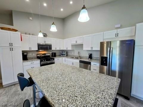 kitchen featuring white cabinets, appliances with stainless steel finishes, a towering ceiling, and decorative light fixtures