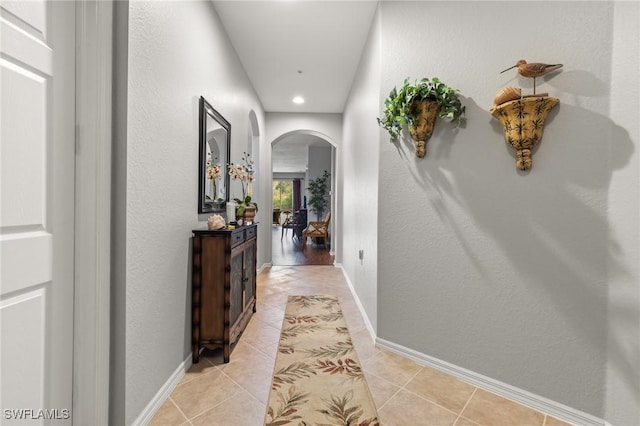 corridor with light tile patterned floors, baseboards, and arched walkways