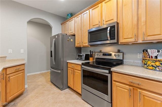14712 Calusa Palms Dr Unit 103, Fort Myers, FL 33919 - kitchen featuring stainless steel appliances, light countertops, arched walkways, light tile patterned flooring, and baseboards