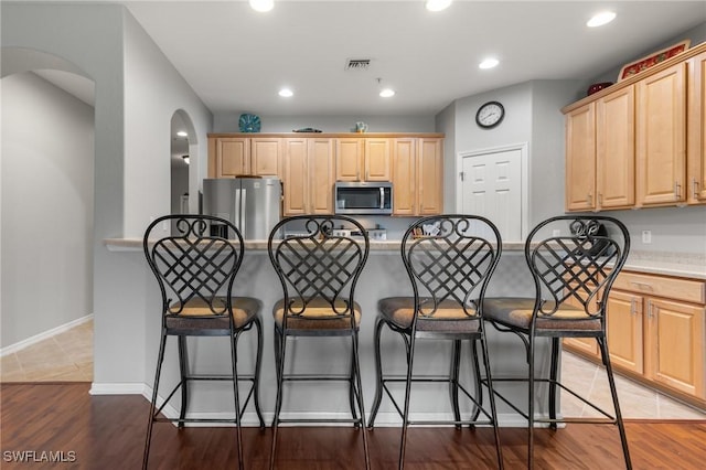 14712 Calusa Palms Dr Unit 103, Fort Myers, FL 33919 - kitchen with stainless steel appliances, light brown cabinets, arched walkways, a breakfast bar area, and light countertops