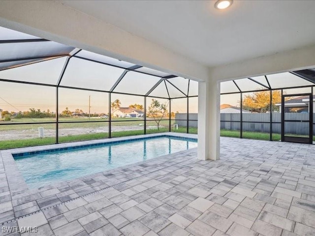 pool at dusk featuring glass enclosure and a patio area