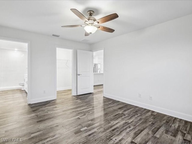 unfurnished bedroom with connected bathroom, a spacious closet, ceiling fan, dark hardwood / wood-style floors, and a closet