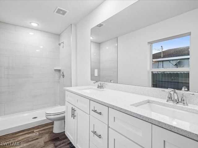 bathroom featuring a tile shower, hardwood / wood-style floors, vanity, and toilet