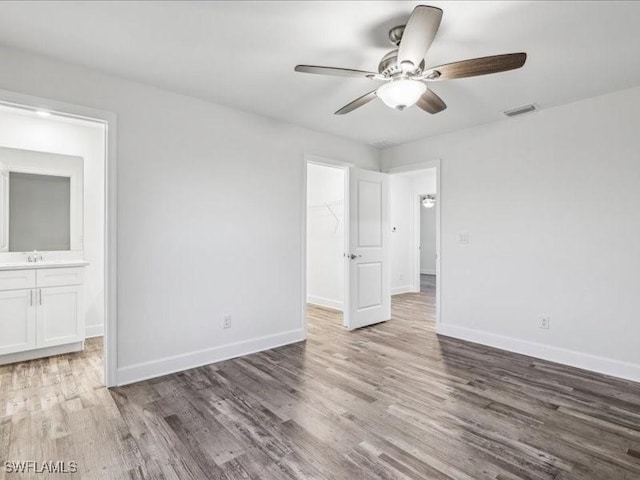 unfurnished bedroom featuring ceiling fan, sink, a spacious closet, a closet, and hardwood / wood-style flooring