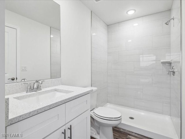 bathroom with tiled shower, hardwood / wood-style floors, vanity, and toilet