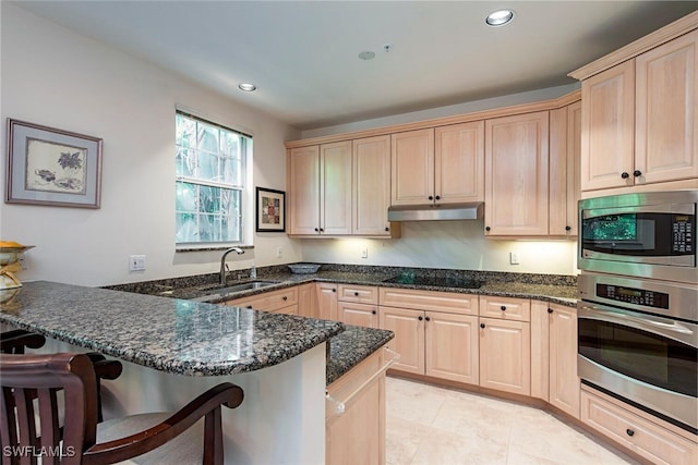 kitchen with under cabinet range hood, stainless steel appliances, a breakfast bar, a peninsula, and a sink