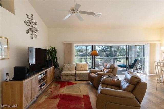 living room with ceiling fan, a towering ceiling, light hardwood / wood-style flooring, and a healthy amount of sunlight