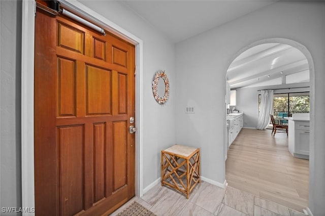 foyer entrance featuring vaulted ceiling with beams and light wood-type flooring