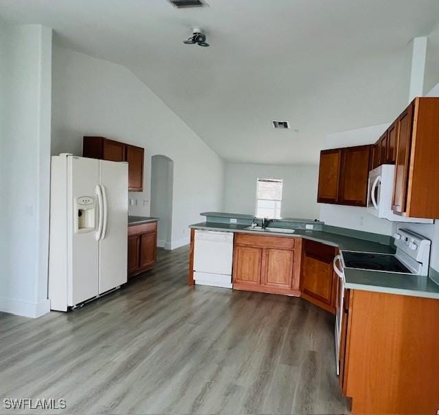 kitchen featuring kitchen peninsula, wood-type flooring, vaulted ceiling, sink, and white appliances