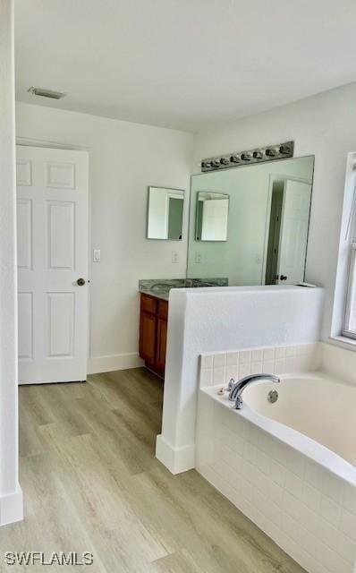 bathroom with hardwood / wood-style flooring, a relaxing tiled tub, and vanity