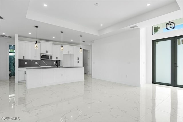 kitchen with white cabinets, a center island with sink, a raised ceiling, sink, and decorative backsplash