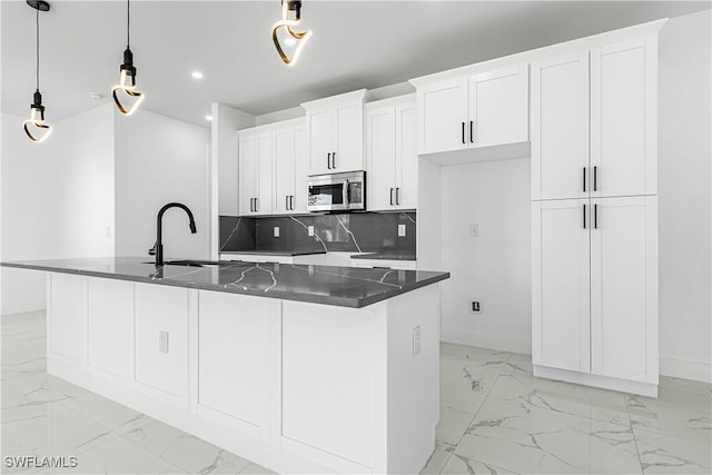 kitchen with white cabinets, decorative light fixtures, a kitchen island with sink, and tasteful backsplash