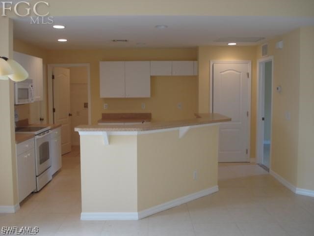 kitchen featuring white cabinets, a kitchen breakfast bar, a kitchen island, and white appliances