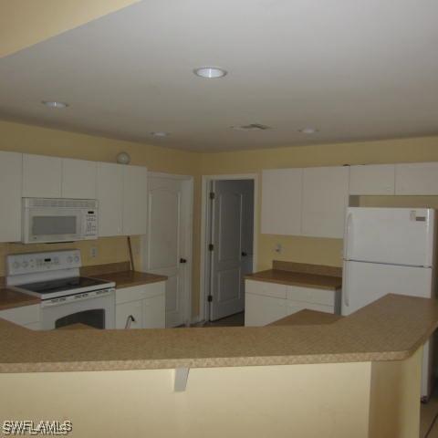 kitchen with white appliances, white cabinetry, and a kitchen island