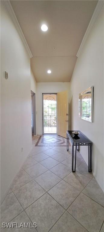 corridor featuring crown molding, light tile patterned flooring, and vaulted ceiling