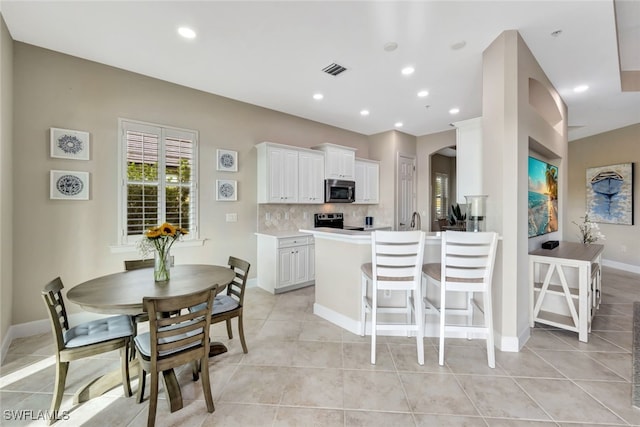 kitchen with kitchen peninsula, decorative backsplash, a kitchen bar, white cabinetry, and stainless steel appliances