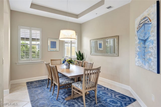 dining area with a tray ceiling, a wealth of natural light, and light tile patterned flooring