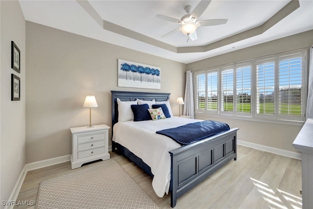 bedroom with light hardwood / wood-style floors, ceiling fan, and a tray ceiling