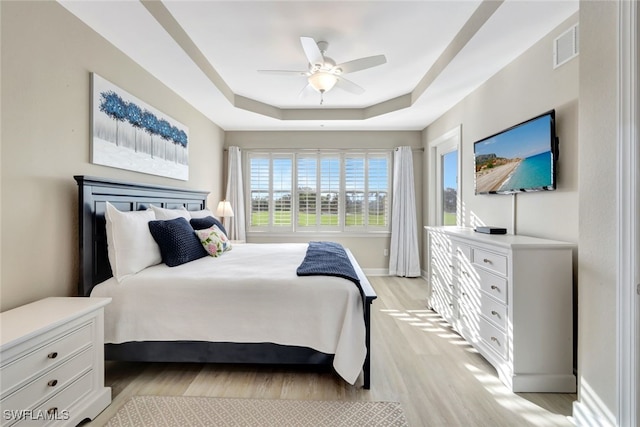 bedroom with a raised ceiling, ceiling fan, and light hardwood / wood-style floors