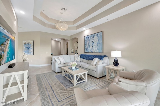 tiled living room featuring a tray ceiling and a notable chandelier