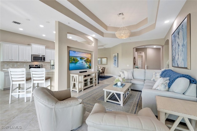 tiled living room with a raised ceiling and an inviting chandelier