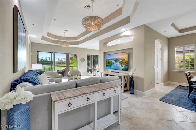 tiled living room featuring a raised ceiling and a chandelier