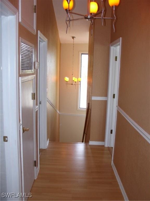 hallway with light wood-type flooring and an inviting chandelier