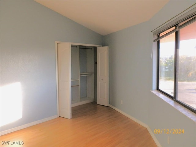 unfurnished bedroom featuring access to exterior, light wood-type flooring, a closet, and lofted ceiling