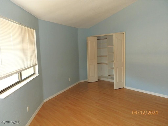 unfurnished bedroom with a closet, lofted ceiling, and hardwood / wood-style flooring