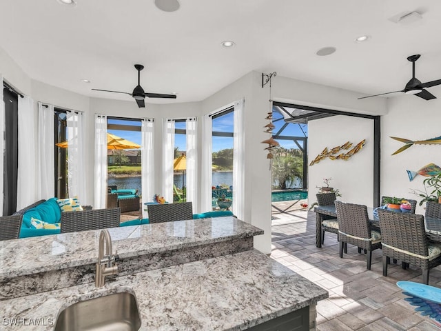 view of patio / terrace with a ceiling fan, outdoor dry bar, a lanai, a water view, and a sink