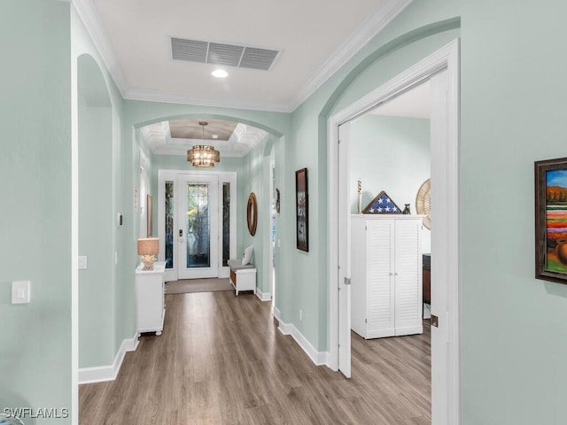 hall featuring arched walkways, crown molding, visible vents, wood finished floors, and baseboards